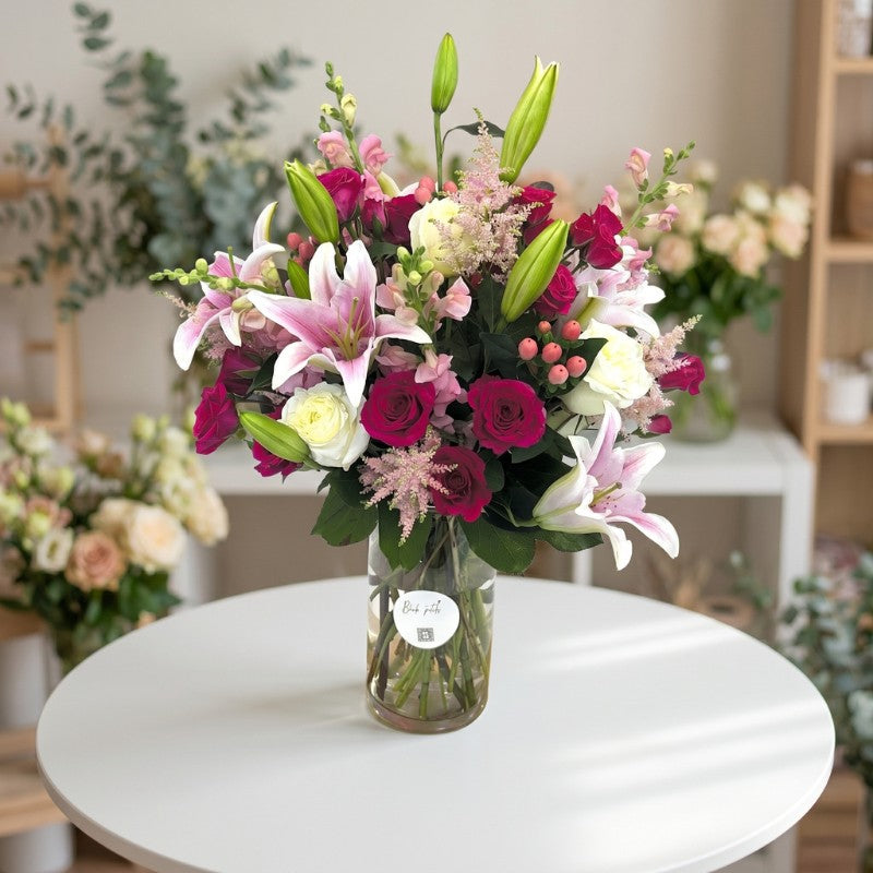 Elegant pink lily and rose floral arrangement in tall glass vase with fresh greenery