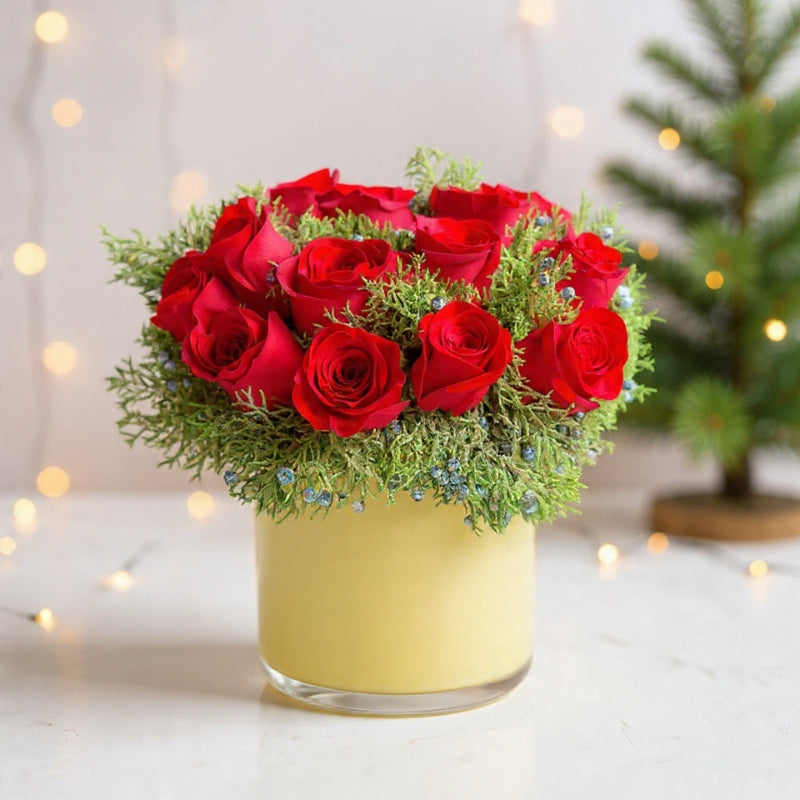 Dome-shaped arrangement of deep red roses with winter greenery in an ivory vase for a luxe winter floral design.