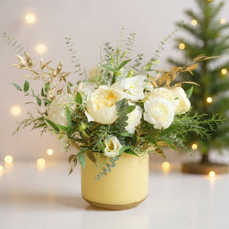 Ivory roses, hydrangeas, gold accents, and winter greenery arranged in a soft white winter vase.