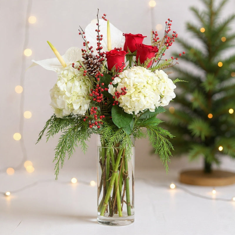 Red roses and white hydrangeas arranged with winter greenery in a clear glass vase for a festive seasonal holiday look today.