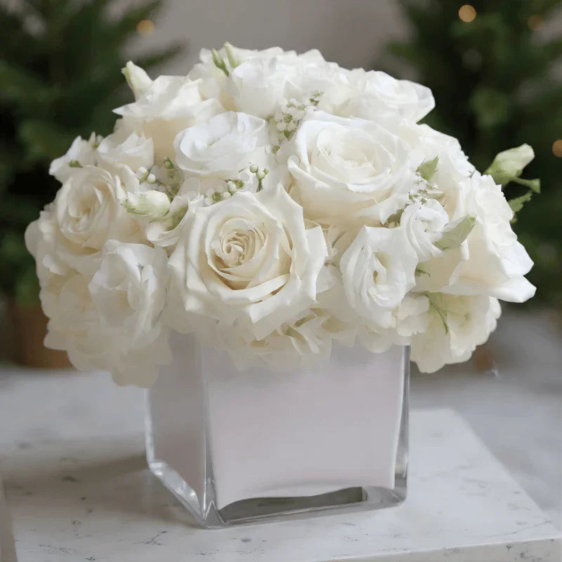 Elegant bouquet of white roses and flowers in clear square glass vase on marble surface