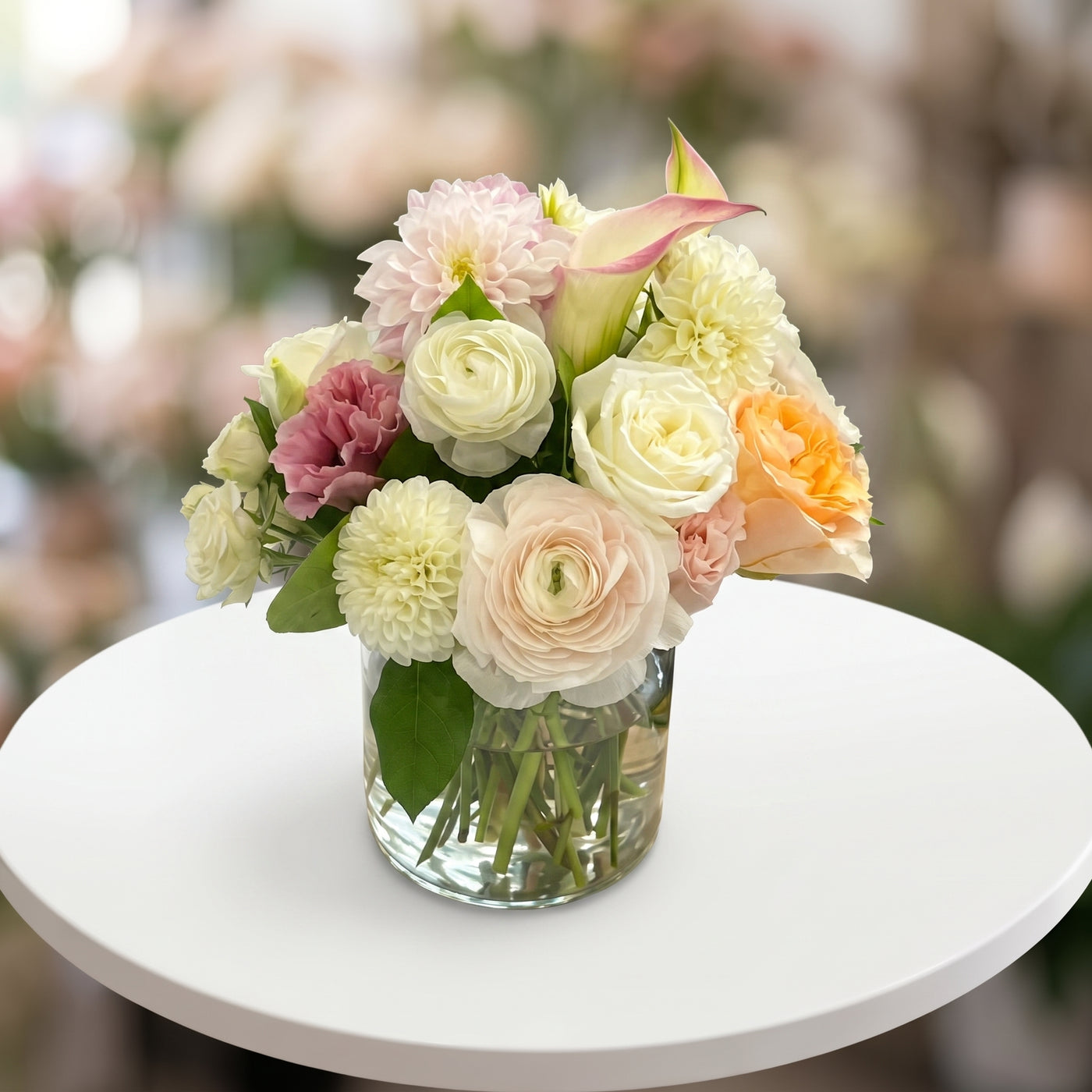 Soft pastel dahlia arrangement with white roses, ranunculus, calla lily and blush flowers in a glass vase
