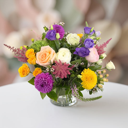 Dahlia Sunset colorful floral arrangement with purple dahlias, peach and orange roses, yellow blooms and seasonal greenery