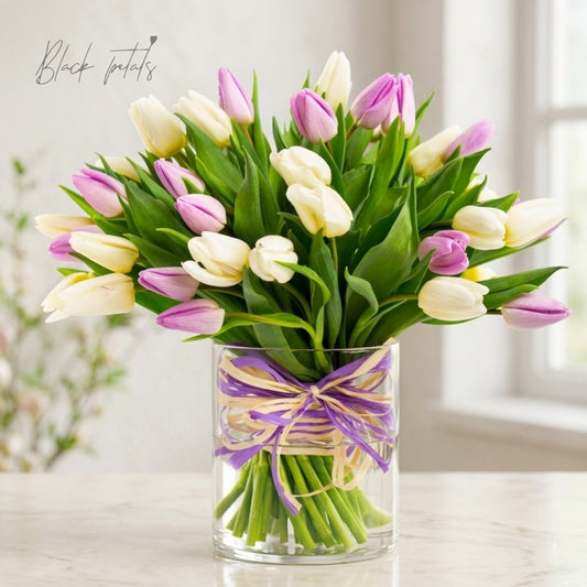 White and light pink tulip bouquet arranged in a clear glass vase with decorative ribbon, displayed on a bright tabletop for an elegant spring floral arrangement.