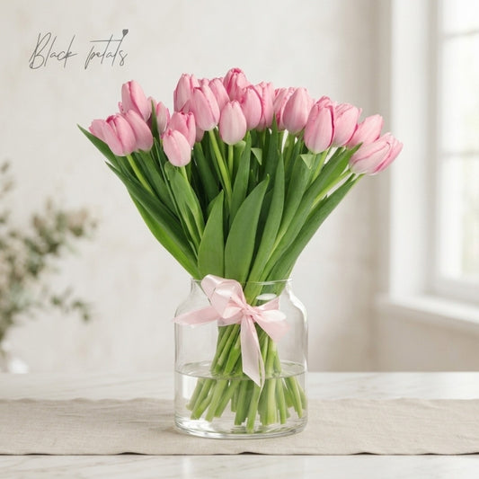 Light pink tulip bouquet arranged in a clear glass vase with a soft pink ribbon, displayed on a neutral table for an elegant spring floral arrangement.