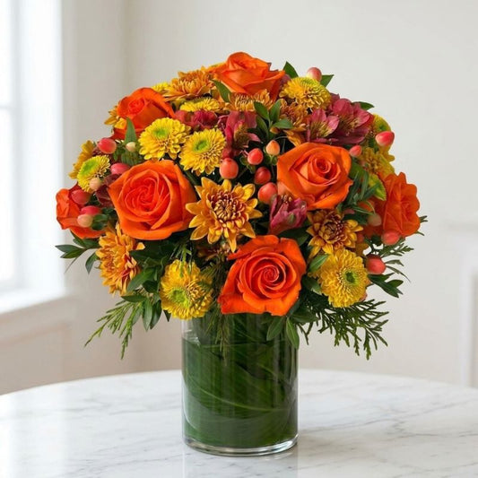 Fall flower arrangement with orange roses, yellow and bronze chrysanthemums, burgundy alstroemeria, coral berries, and greenery in a leaf-lined glass vase.