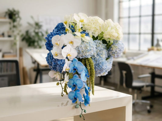 Luxurious blue and white floral arrangement featuring vibrant blue and soft blue hydrangeas, cascading blue and white orchids, creamy white blooms, and trailing green amaranthus in an elegant vase.