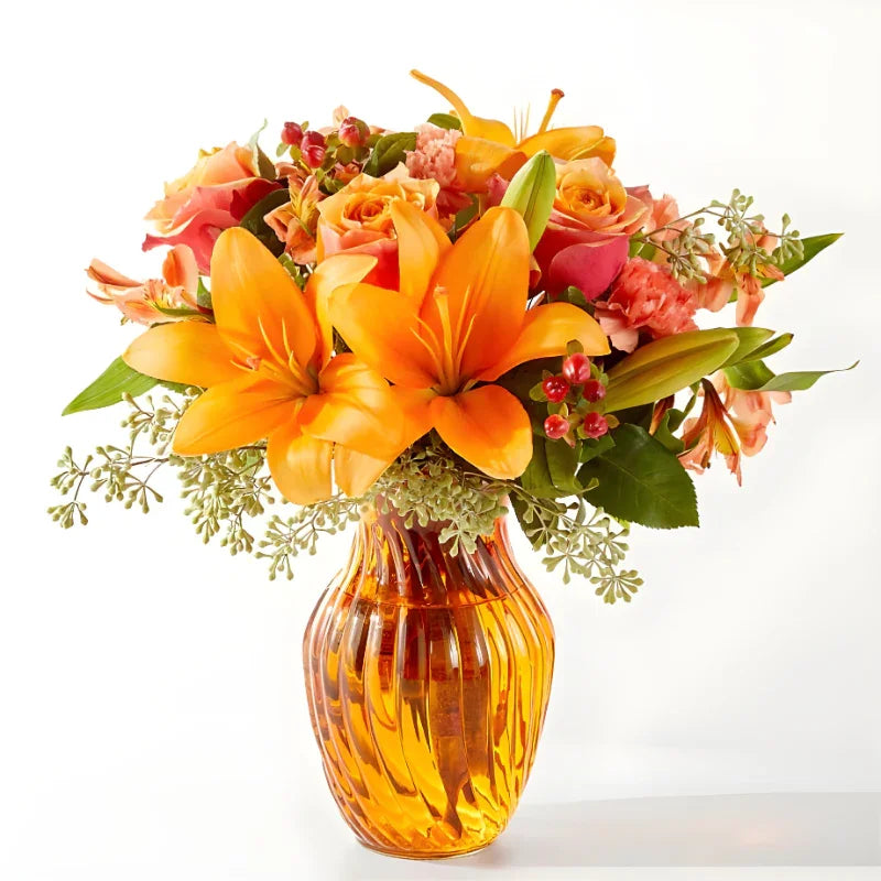 Bright orange lilies and peach roses arranged in a ribbed amber glass vase with greenery