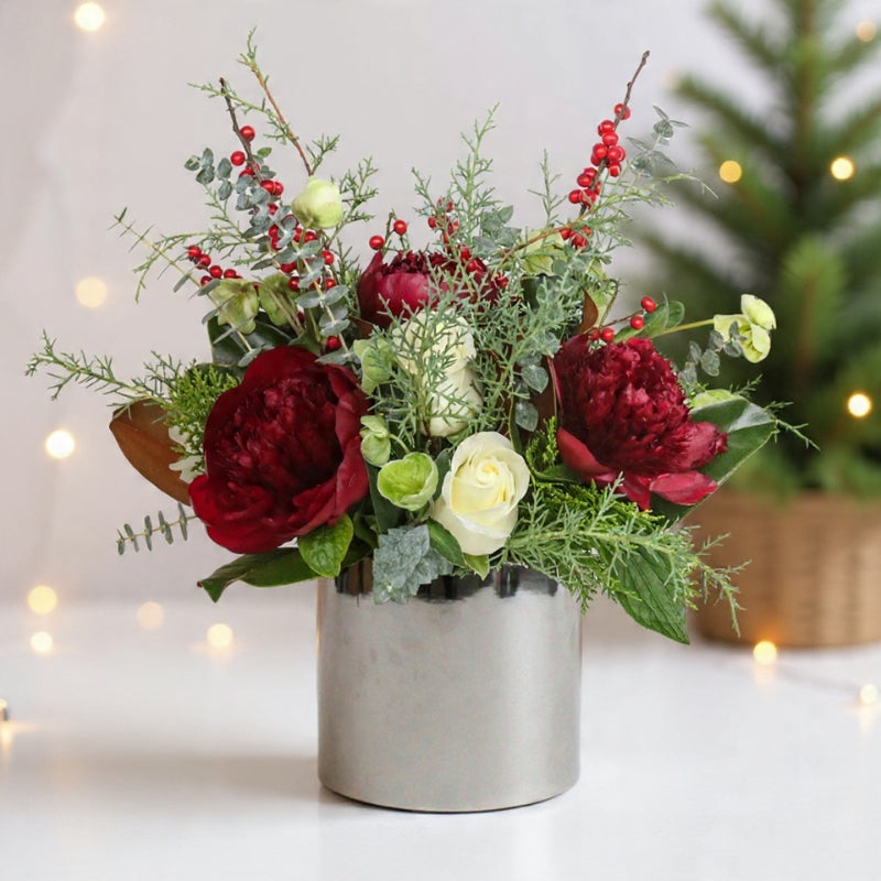 Burgundy blooms, ivory roses, berries, and winter greenery arranged in a modern vase for a rich winter look.