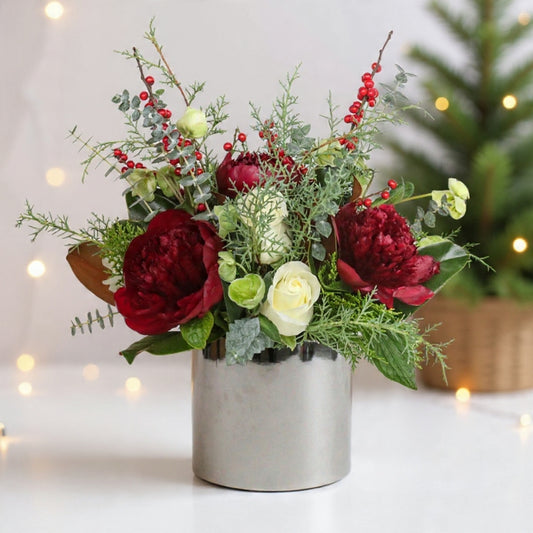 Burgundy blooms, ivory roses, berries, and winter greenery arranged in a modern vase for a rich winter look.