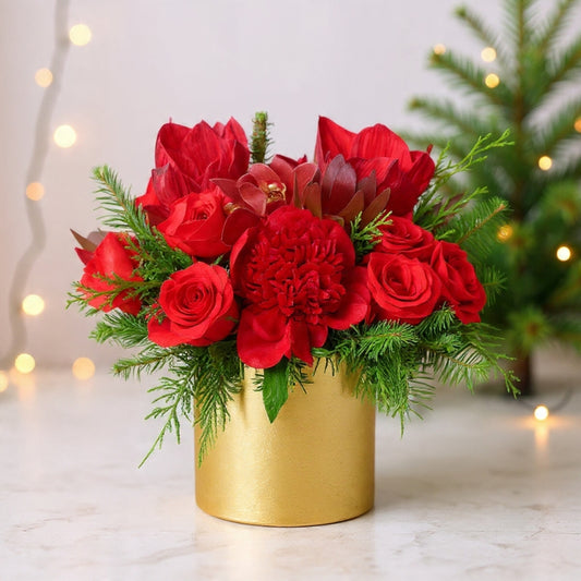 Red roses and orchids arranged in a gold vase with winter greenery for a luxurious holiday floral centerpiece.