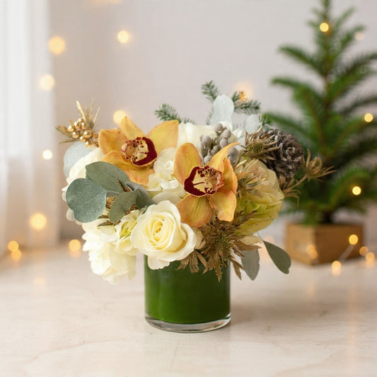 Ivory roses and cymbidium orchids with pinecones and soft winter greenery arranged for an elegant gold-accent winter bouquet.