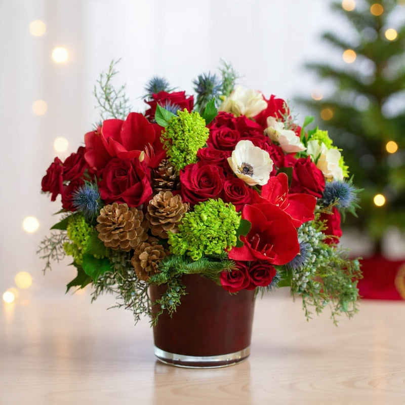 Large centerpiece of red roses, anemones, pinecones, berries, and winter greenery arranged for a grand festive holiday display.