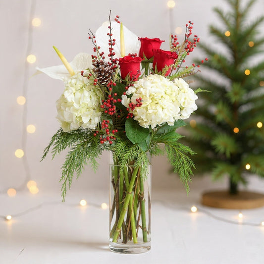 Red roses and white hydrangeas arranged with winter greenery in a clear glass vase for a festive seasonal holiday look today.