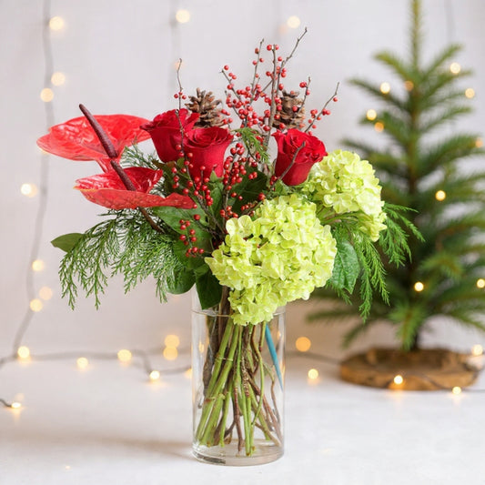 Red roses and white hydrangeas arranged with winter greenery in a clear vase for a festive Christmas holiday floral display.