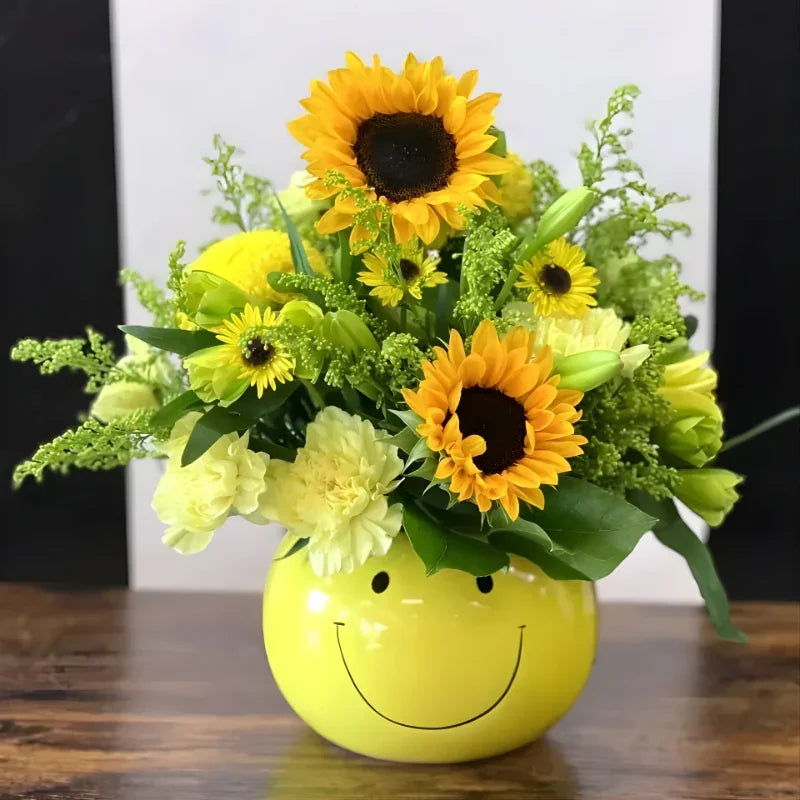 Happy bouquet with sunflowers and yellow flowers in a smiley face yellow ceramic vase on wooden table