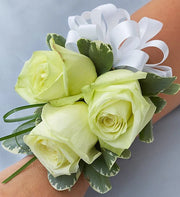 White rose corsage with three blooms and variegated green leaves, accented by a white ribbon bow on wrist