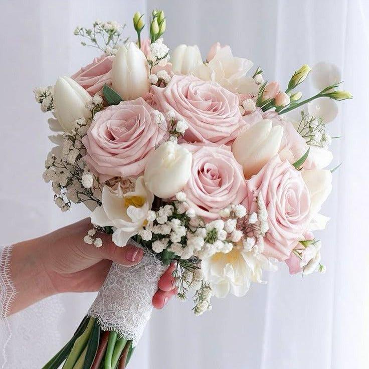 Bridal bouquet with blush pink roses, white tulips, and baby's breath held against a light background