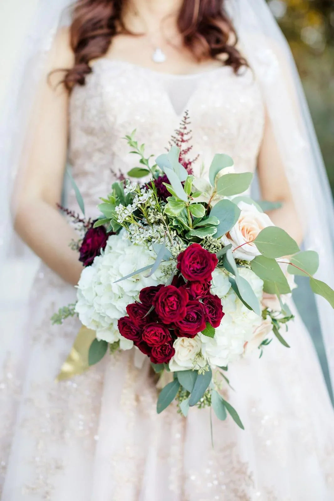 Bridal bouquet with burgundy roses, white flowers, greenery, held by bride in lace wedding dress