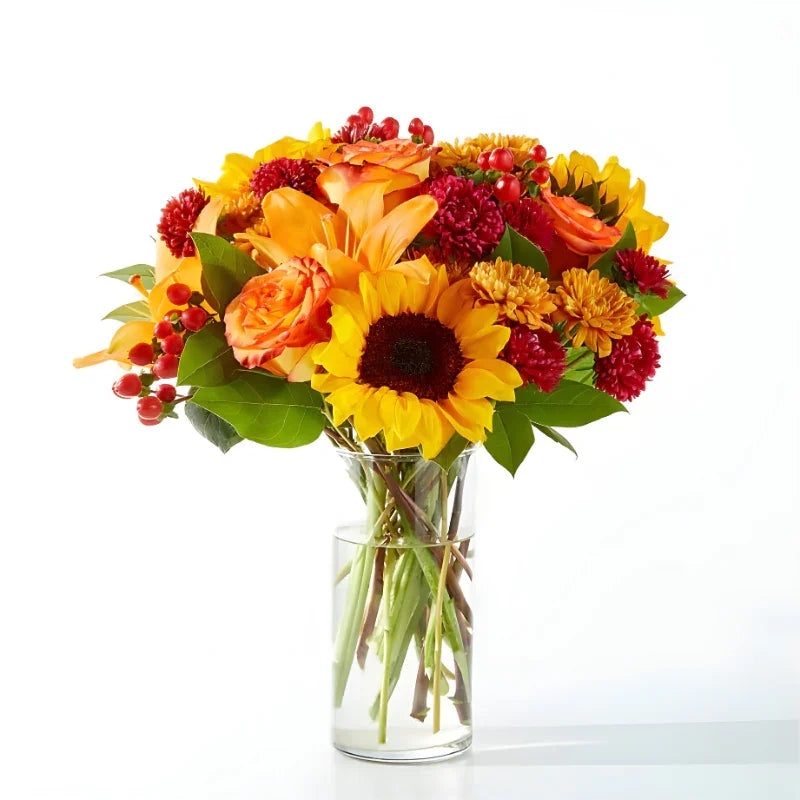 Bright fall bouquet with sunflowers, orange roses, red berries, and autumn chrysanthemums in clear glass vase