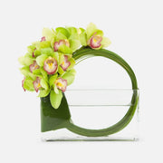 Modern floral arrangement of green cymbidium orchids in a circular design inside a rectangular glass vase