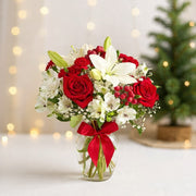 Holiday bouquet with red roses, white lilies, berries, and seasonal greens arranged in a glass vase with a red ribbon.