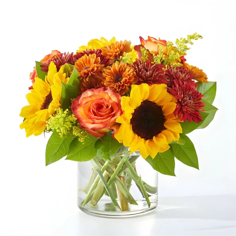 Autumn bouquet with sunflowers, orange roses, chrysanthemums, green leaves in clear glass vase