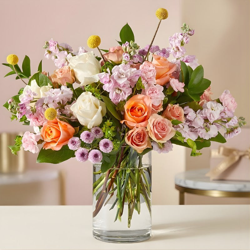 French Market mixed flower bouquet with peach roses, white roses, pink stock flowers and greenery in a clear glass vase