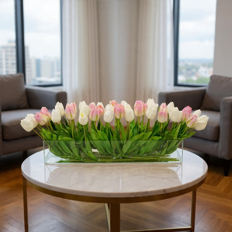 Blush pink and white tulip lobby arrangement in a rectangular glass vase on a marble coffee table in a modern office lobby.