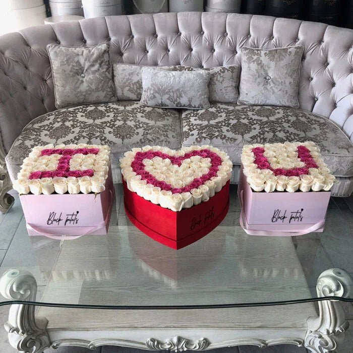 Elegant floral arrangement spelling I heart U with pink and white roses on glass table in front of tufted sofa