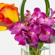 Close-up of vibrant purple orchids and a yellow-orange calla lily in a clear glass vase