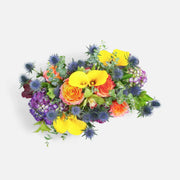 Colorful floral arrangement with yellow calla lilies, orange roses, purple hydrangeas, blue thistles, and green foliage
