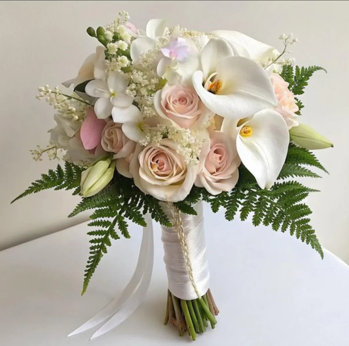 Elegant bridal bouquet with white orchids, blush roses, greenery, and wrapped satin ribbon