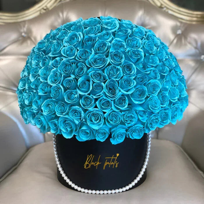 Large bouquet of vibrant blue roses in black box with pearl chain on tufted beige chair