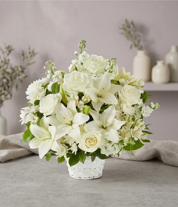 Elegant white flower arrangement with lilies, roses, and greenery in a woven basket