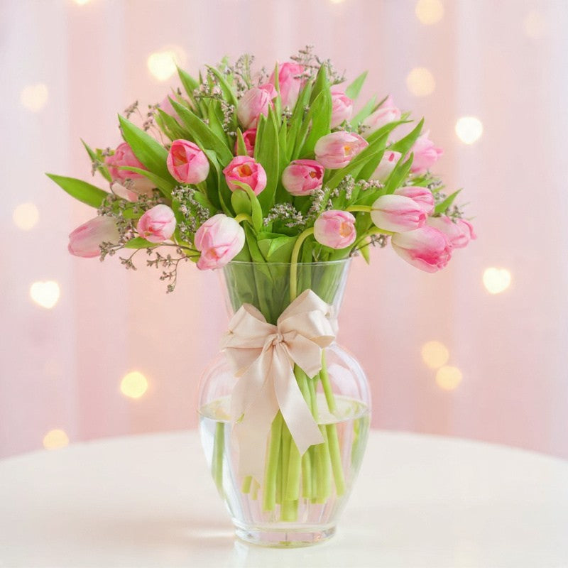 Soft blush pink tulips arranged in a clear glass vase with greenery