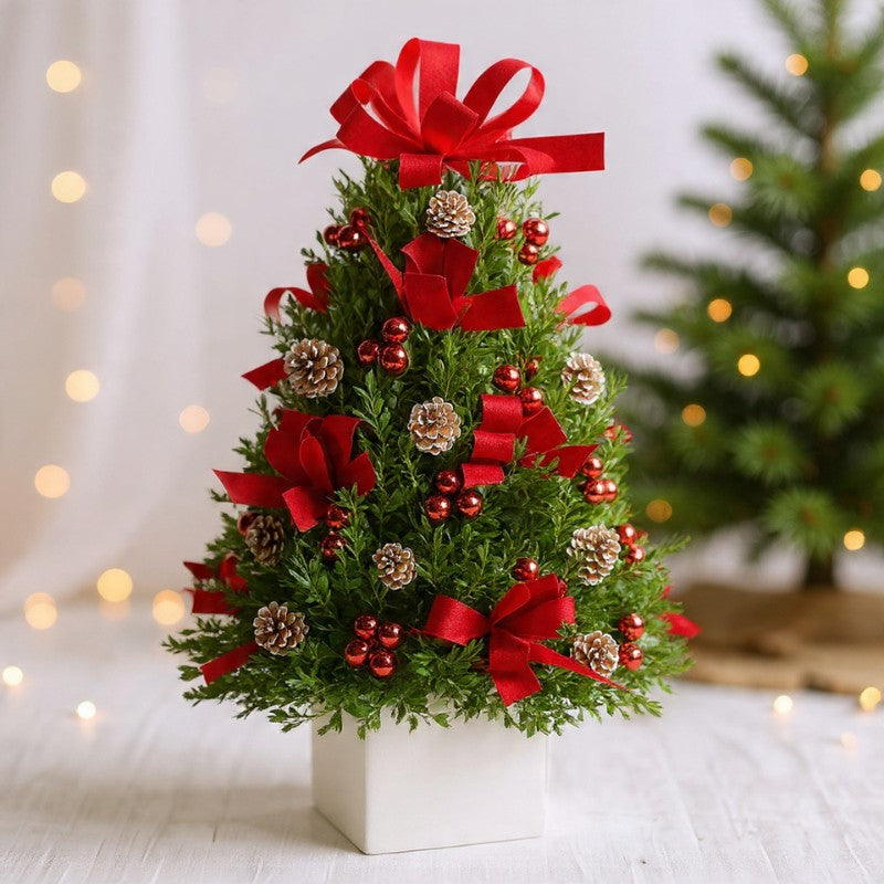 Mini holiday tree with red bows, berries, and frosted pinecones in a white base, perfect for classic Christmas décor and gifting.