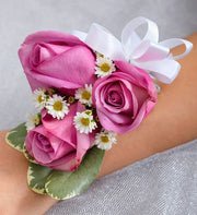Purple rose corsage with white daisies and green leaves, tied with a white ribbon on wrist