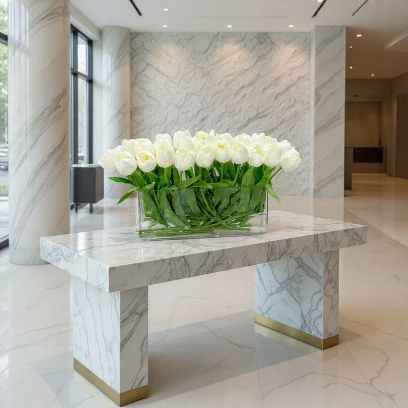 Luxury white tulip lobby arrangement in a rectangular glass vase displayed on a marble table in a modern hotel lobby