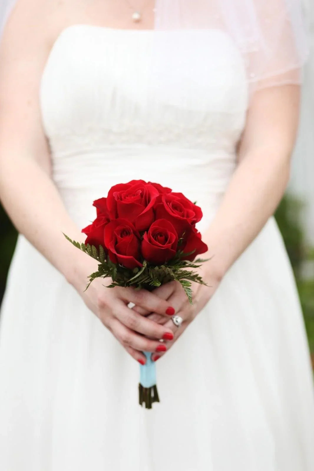 Bride in white wedding dress holding a bouquet of red roses with green foliage
