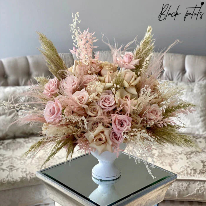 Elegant bouquet of blush roses and dried pampas grass in white vase on mirrored table
