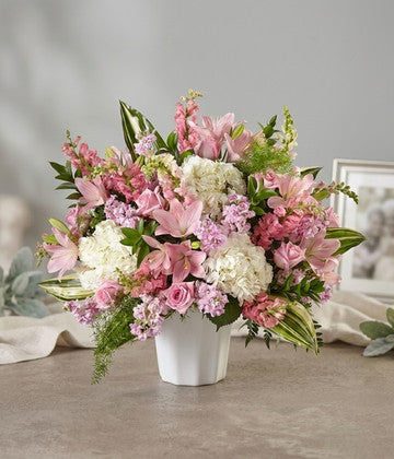Elegant floral arrangement with pink lilies, roses, white hydrangeas, and green leaves in a white vase
