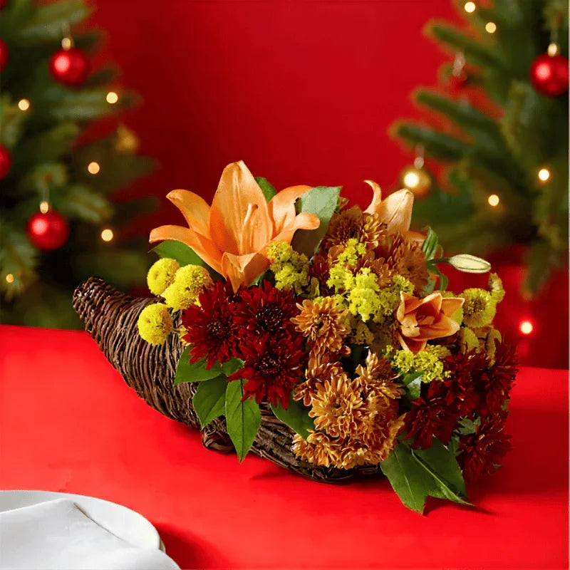 Autumn floral arrangement with orange lilies, red and yellow flowers in wicker cornucopia on red table