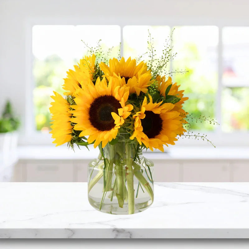 Bright sunflower bouquet in clear glass vase on marble countertop with bright window background