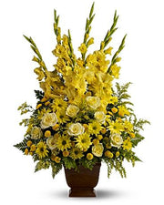 Elegant yellow floral arrangement with gladiolus, roses, daisies, and greenery in a brown vase