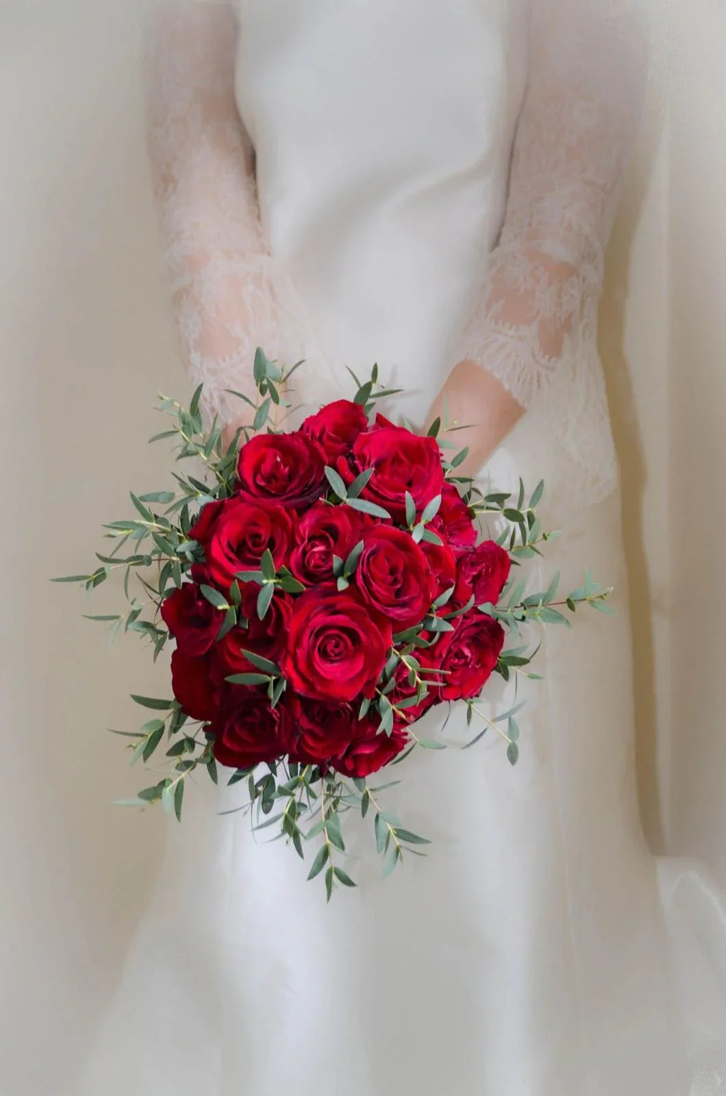 Bride in white dress holding a cascading bouquet of deep red roses with greenery