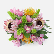 Vibrant bouquet with pink protea, orchids, green foliage, and yellow pincushion flowers on white