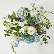 Sympathy floral arrangement with white roses, blue hydrangeas, white lilies, snapdragons, and greenery