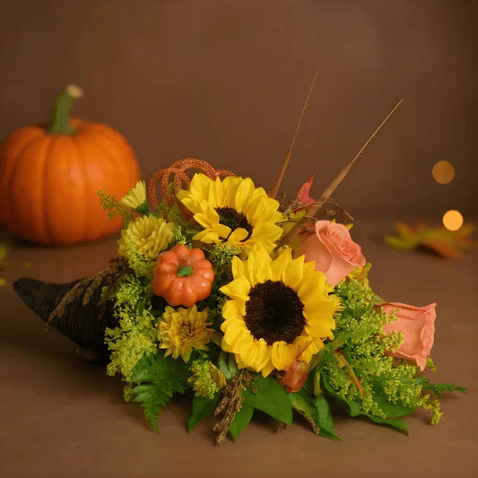 Thanksgiving cornucopia with sunflowers, roses, mini pumpkin, and autumn foliage on brown background